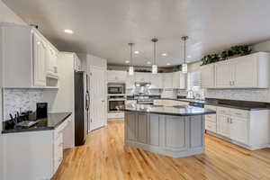 Kitchen with white cabinets, stainless steel appliances, decorative light fixtures, and a center island