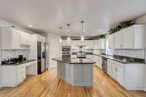 Kitchen with light wood-type flooring, white cabinets, decorative light fixtures, and appliances with stainless steel finishes