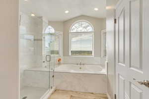 Upgraded master bathroom featuring shower with separate bathtub, LVP flooring, and vaulted ceiling