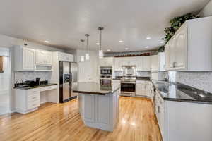 Kitchen featuring stainless steel appliances, hardwood floors, a center island, white cabinets, and pendant lighting