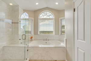 Upgraded master bathroom featuring french-style door shower with separate jetted tub, LVP flooring, and vaulted ceiling