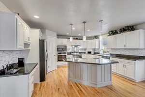 Kitchen with appliances with stainless steel finishes, pendant lighting, a kitchen island, white cabinets, and light wood-type flooring