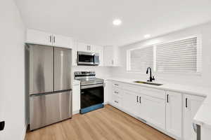 Kitchen featuring white cabinets, light hardwood / wood-style floors, sink, and appliances with stainless steel finishes