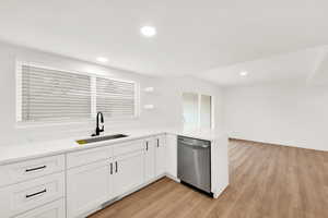 Kitchen with white cabinetry, light wood-type flooring, sink, stainless steel dishwasher, and kitchen peninsula