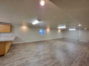 Basement with a healthy amount of sunlight, light wood-type flooring, and a textured ceiling