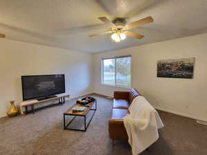 Living room featuring a textured ceiling, dark carpet, and ceiling fan