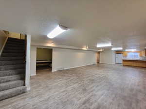 Basement with white fridge with ice dispenser, a textured ceiling, and wood-type flooring