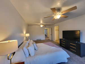 Carpeted bedroom featuring a textured ceiling, ceiling fan, a walk in closet, and a closet