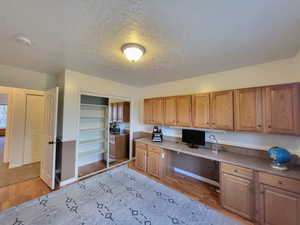 Home office featuring a textured ceiling, built in desk, and light hardwood / wood-style floors