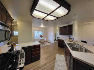 Kitchen featuring dark brown cabinetry, a textured ceiling, sink, and light wood-type flooring