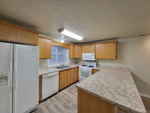 Kitchen with light wood-type flooring, a textured ceiling, white appliances, sink, and kitchen peninsula