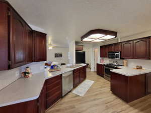 Kitchen featuring kitchen peninsula, light hardwood / wood-style flooring, a textured ceiling, sink, and appliances with stainless steel finishes