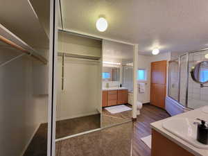 Bathroom with a textured ceiling, wood-type flooring, vanity, a shower with shower door, and toilet