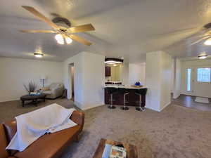 Living room featuring a textured ceiling, ceiling fan, and carpet floors