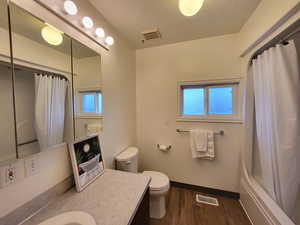 Full bathroom with wood-type flooring, toilet, a textured ceiling, vanity, and shower / bathtub combination with curtain