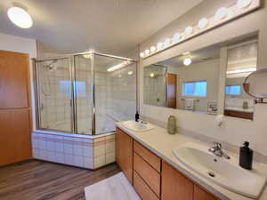 Bathroom featuring vanity, hardwood / wood-style floors, bath / shower combo with glass door, and a textured ceiling