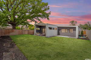 Back house at dusk with a lawn and a patio