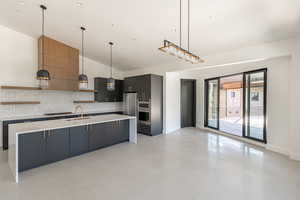 Kitchen featuring decorative light fixtures, vaulted ceiling, a kitchen island with sink, and tasteful backsplash