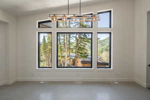 Empty room featuring a notable chandelier, plenty of natural light, concrete flooring, and vaulted ceiling