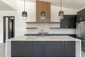 Kitchen featuring stainless steel appliances, vaulted ceiling, hanging light fixtures, and an island with sink