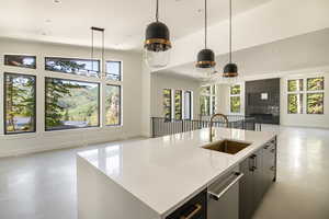 Kitchen with pendant lighting, a center island with sink, sink, stainless steel dishwasher, and a fireplace