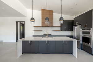 Kitchen featuring stainless steel appliances, tasteful backsplash, pendant lighting, lofted ceiling, and a kitchen island with sink