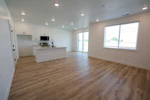 Kitchen with stainless steel appliances, light hardwood / wood-style floors, a center island with sink, sink, and white cabinets