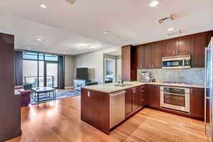 Kitchen featuring kitchen peninsula, light hardwood / wood-style flooring, sink, tasteful backsplash, and appliances with stainless steel finishes