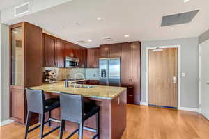 Kitchen featuring stainless steel appliances, light hardwood / wood-style floors, sink, kitchen peninsula, and a kitchen bar