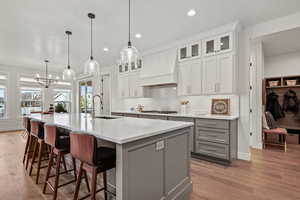 Kitchen with a large island with sink, sink, hanging light fixtures, and light hardwood / wood-style floors