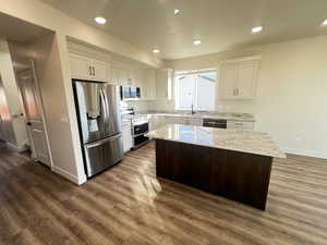 Kitchen with stainless steel appliances, white cabinetry, dark hardwood / wood-style floors, light stone countertops, and a center island