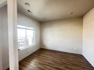 Spare room with dark wood-type flooring and lofted ceiling