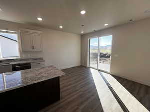 Kitchen with dark wood-type flooring, light stone countertops, stainless steel dishwasher, and white cabinetry