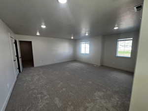 Empty room with a healthy amount of sunlight, a textured ceiling, and dark carpet