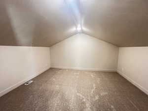 Bonus room with a textured ceiling, lofted ceiling, and dark carpet