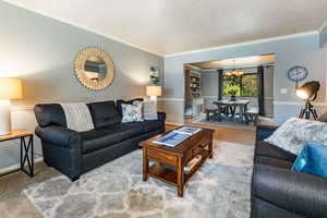 Living room featuring a textured ceiling, an inviting chandelier, crown molding, and carpet