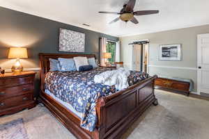 Carpeted bedroom with a barn door, ceiling fan, and crown molding