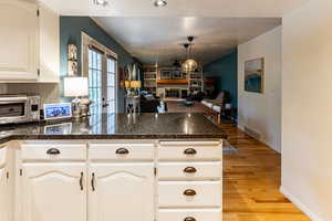 Kitchen featuring light hardwood / wood-style floors, pendant lighting, kitchen peninsula, white cabinetry, and dark stone countertops