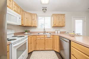 Kitchen featuring light brown cabinets, white appliances, light tile patterned floors, and sink