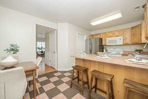 Kitchen with sink, light brown cabinetry, a kitchen bar, white appliances, and dark hardwood / wood-style flooring