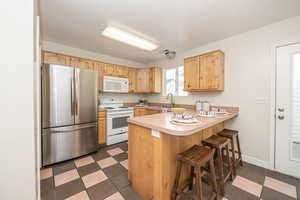 Kitchen with white appliances, light brown cabinetry, sink, a kitchen breakfast bar, and kitchen peninsula