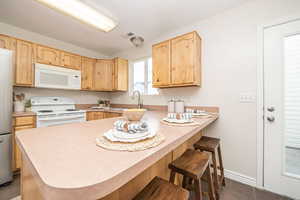 Kitchen featuring a kitchen bar, kitchen peninsula, sink, light brown cabinetry, and white appliances