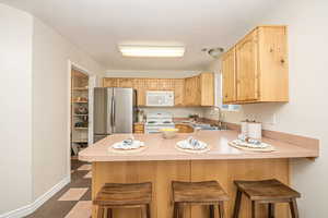 Kitchen with light brown cabinetry, sink, white appliances, and a breakfast bar