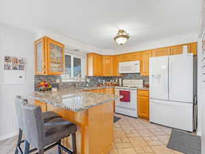 Kitchen featuring light stone counters, a kitchen bar, white appliances, decorative backsplash, and kitchen peninsula