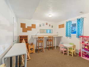 Recreation room featuring carpet and a textured ceiling