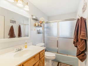 Full bathroom with toilet, combined bath / shower with glass door, vanity, and tile patterned flooring