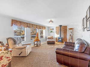 Living room with a wood stove, a textured ceiling, carpet floors, and a healthy amount of sunlight