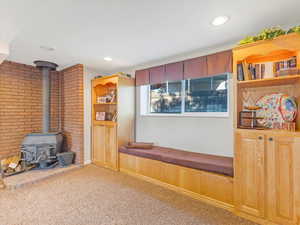 Living room featuring carpet flooring, brick wall, and a wood stove