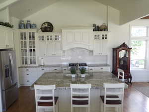 Kitchen featuring stainless steel fridge, a kitchen island with sink, lofted ceiling, and a breakfast bar area