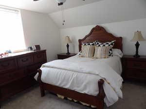 Carpeted bedroom with ceiling fan and vaulted ceiling